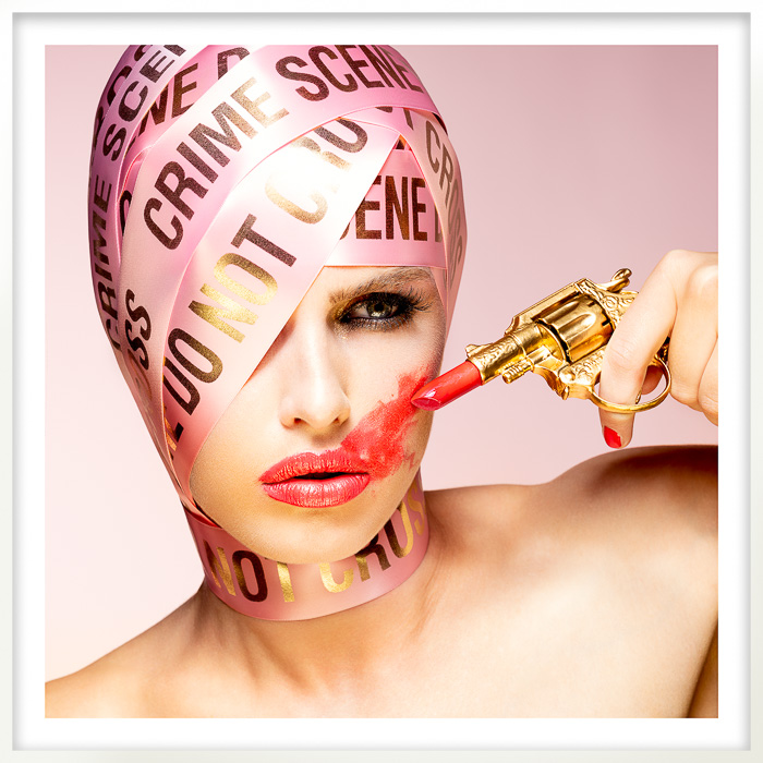 Crime scene fashion portrait of a woman with a lipstick gun, symbolizing power, beauty, and violence in a bold image.