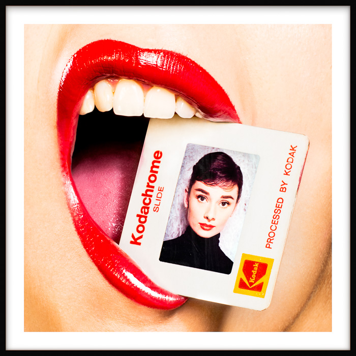 Audrey Hepburn Kodachrome artwork of a stylish woman with red lips holding a photo of the iconic actress gently between her teeth.