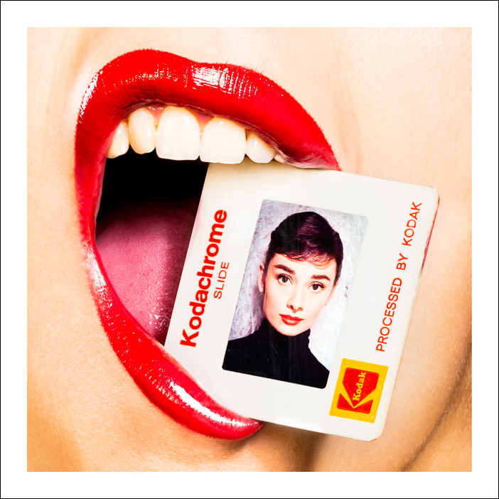 Audrey Hepburn Kodachrome artwork of a stylish woman with red lips holding a photo of the iconic actress gently between her teeth.