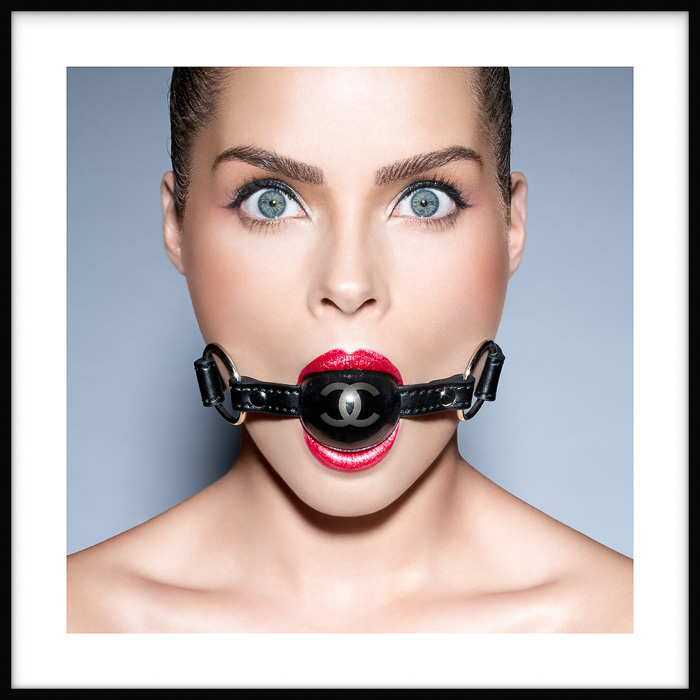 Framed photo artwork of wide-eyed looking young woman with CC logo ball gag in mouth, fastened with black leather straps.