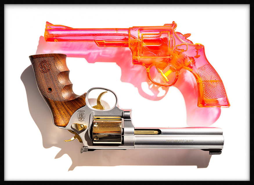 TOY AND TRIGGER: A pink translucent toy-like gun hovers above an upside-down Smith & Wesson Magnum revolver on a plain background.