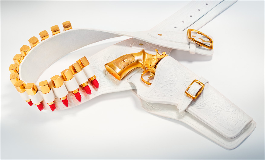 White leather holster belt with gold Chanel lipsticks and revolver against cool pink: an iconic fashionweapon of luxe and femme power.