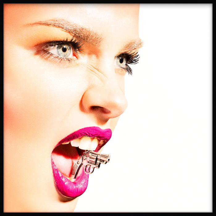 Striking fashion portrait of a young fierce woman with tiny revolver clenched in her mouth, exuding fierce elegance.