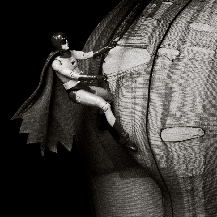 Batman action figure surreal art: climbing into torn tights at night, deconstructing the heroic archetype in pop culture art.