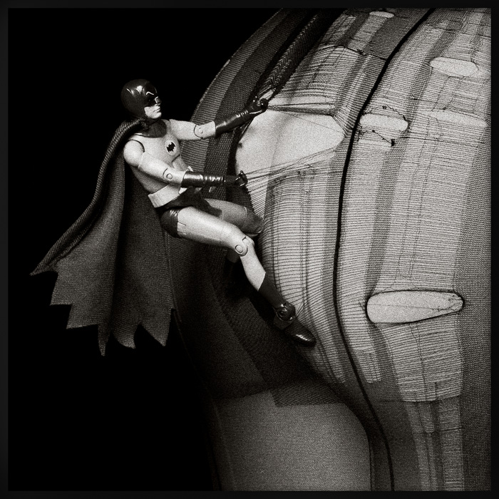Batman action figure surreal art: climbing into torn tights at night, deconstructing the heroic archetype in pop culture art.