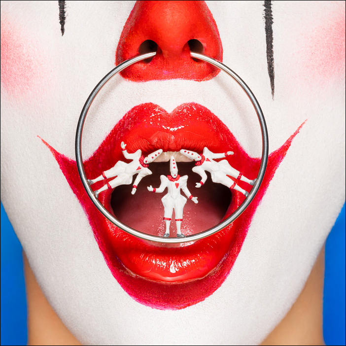 Surreal clown with Pierrots nose ring, balancing in dramatic tension, exploring performance, rivalry and line between humor and danger.