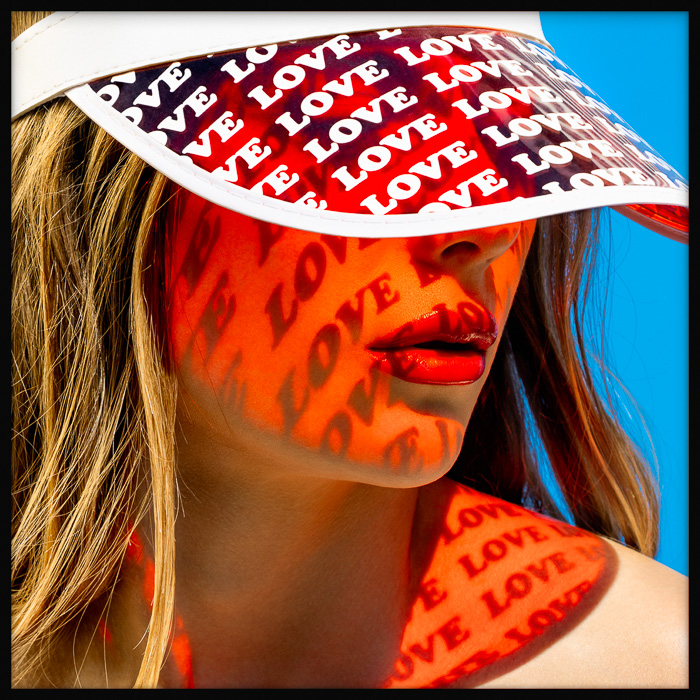 Red love projection on skin, radiant sunlight casting patterns of the word love on a woman's face and shoulder, creating summer vibes.