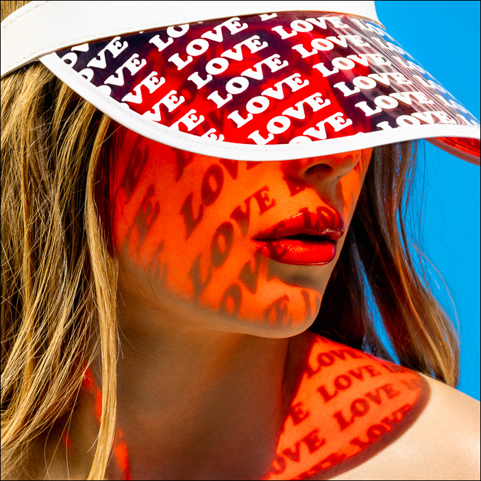 Red love projection on skin, radiant sunlight casting patterns of the word love on a woman's face and shoulder, creating summer vibes.