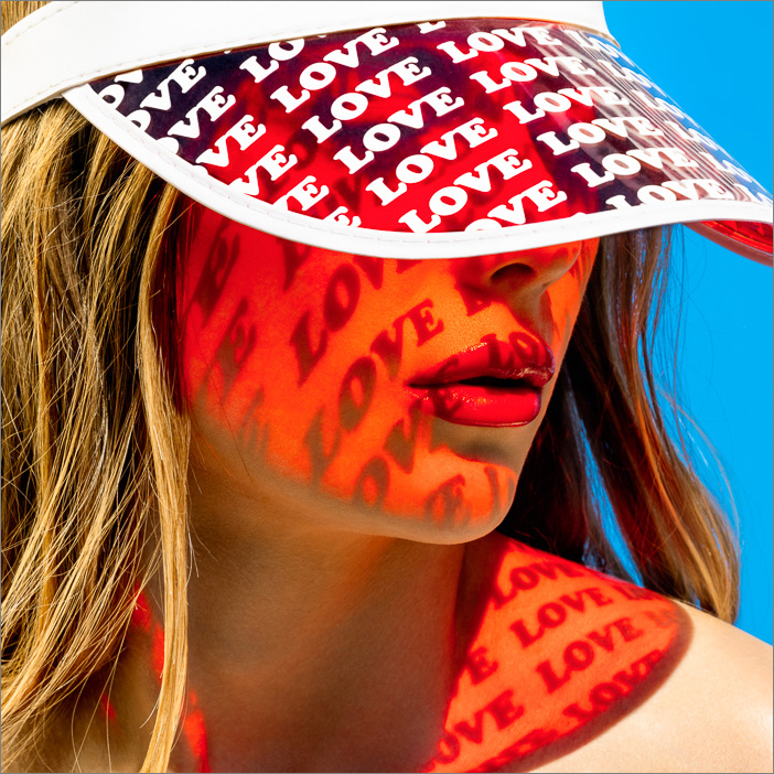 Sunlight projects a pattern of the words love on the skin of a girl wearing a red transparent sun visor covered with this love print.